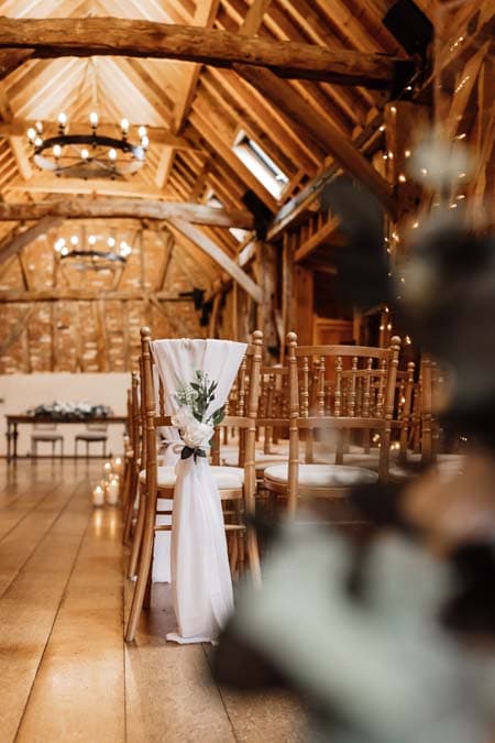 A barn ceremony aisle dressed with chair drapes, florals and candlelight by Events By Beau