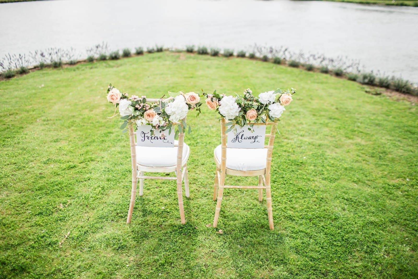 Two decorated chairs set out on a lawn beside a lake