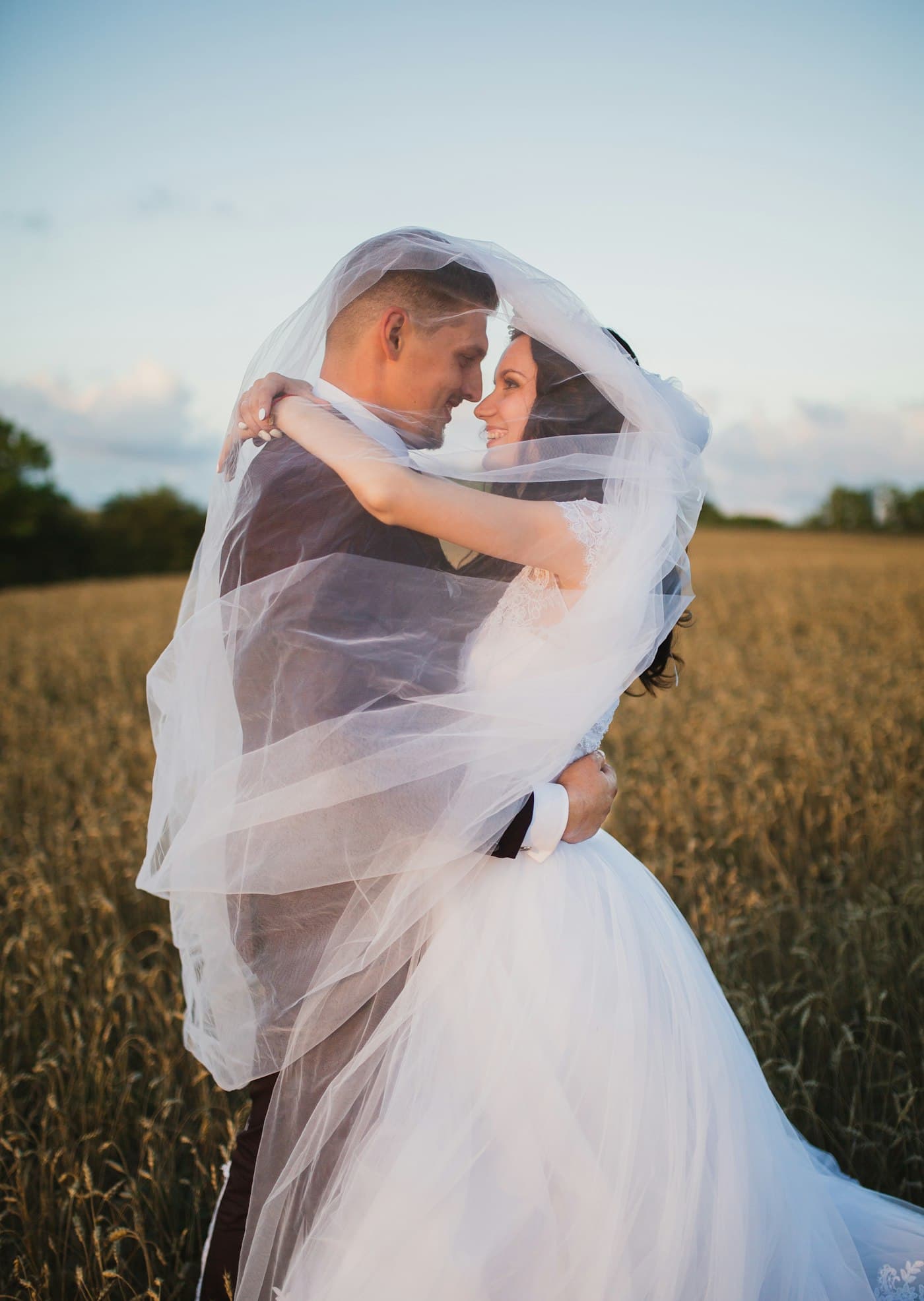 A couple beneath a veil in an open field